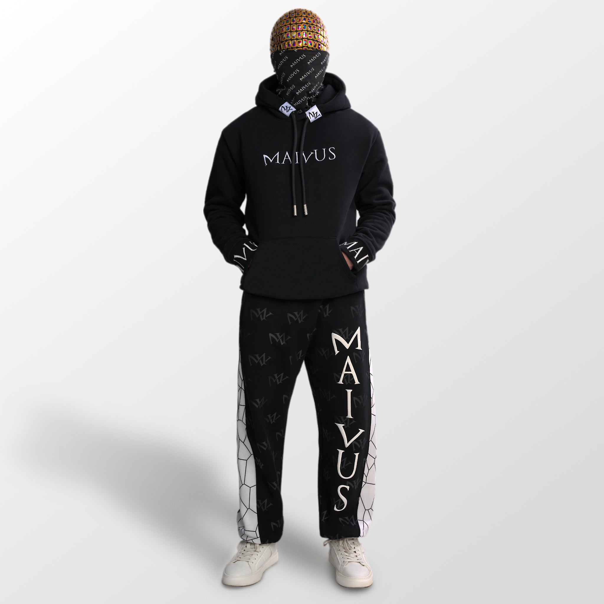 Model wearing a luxury black and white hoodie and joggers. 'MV' branding on joggers with geometric shapes and white embroidery on hoodie from 'MAIVUS' against a white studio