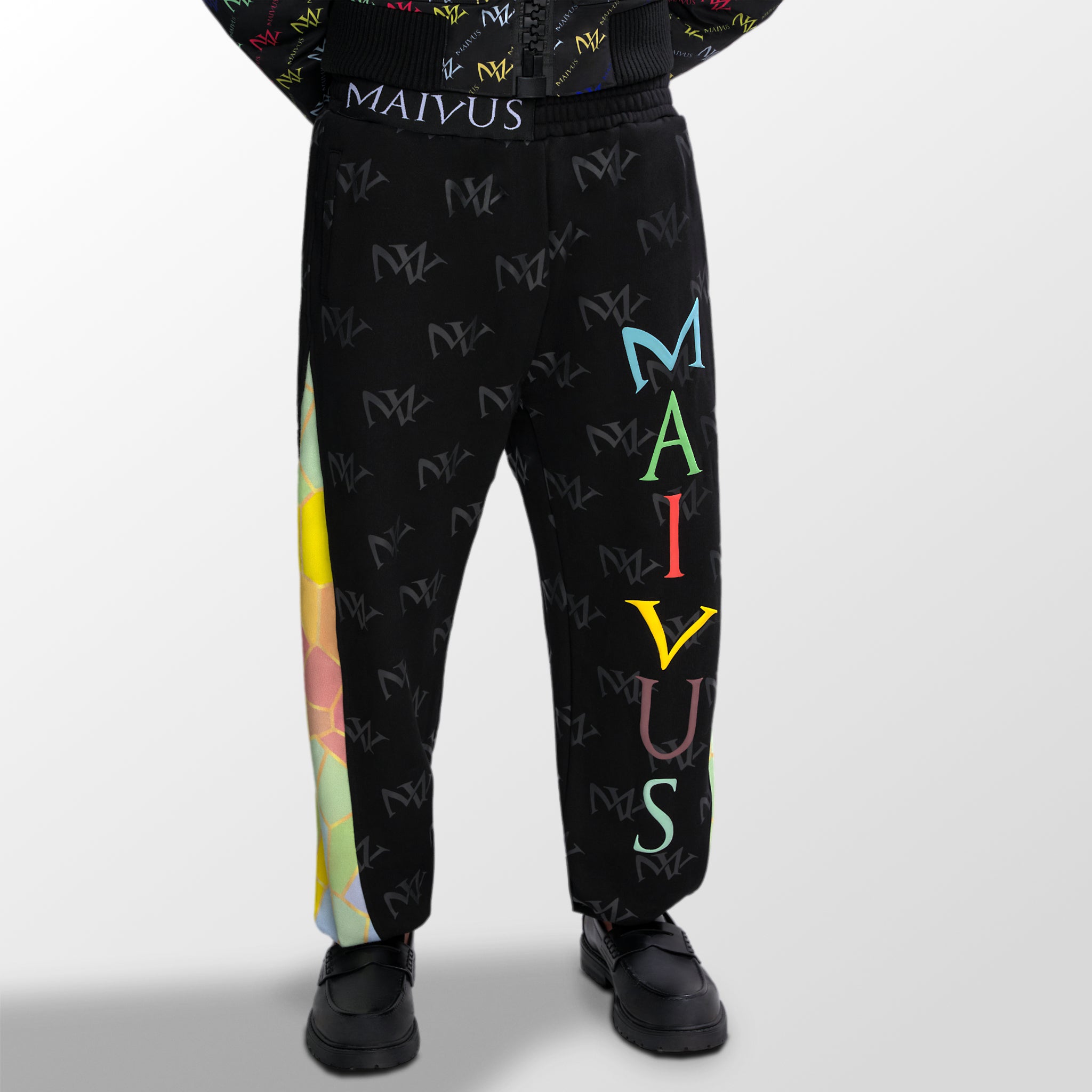 Model wearing the luxury multicolored joggers with 'MV' branding and geometric shapes from 'MAIVUS' against a white studio backdrop