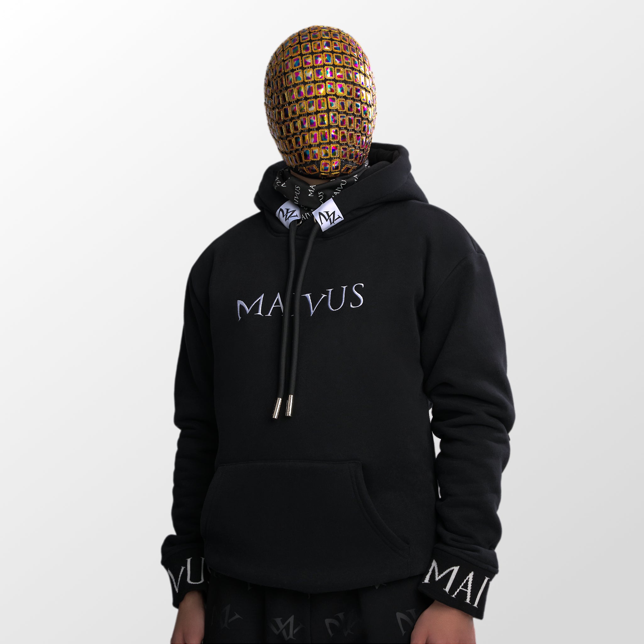 Model wearing a luxury black and white hoodie with white embroidery and branded snood from 'MAIVUS' against a white studio backdrop