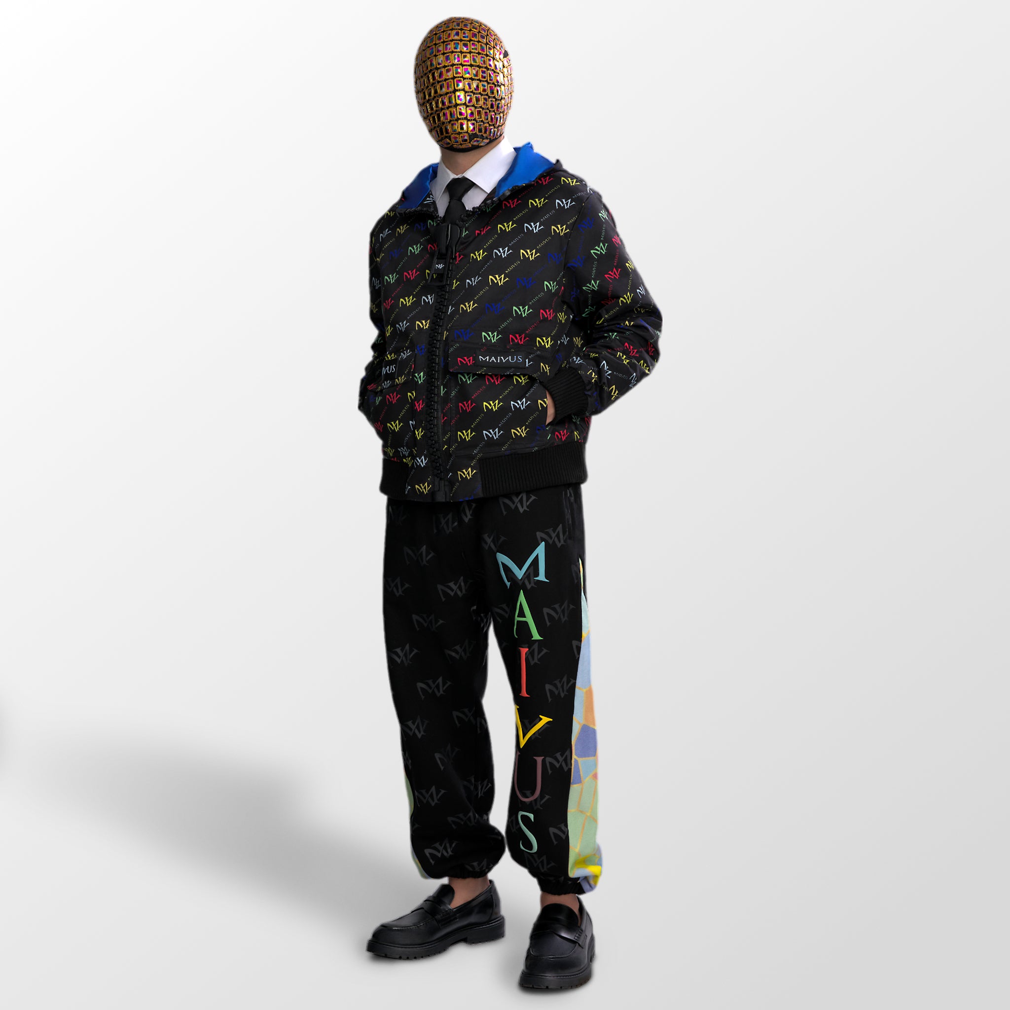 Model wearing the luxury multicolored jacket and joggers with 'MV' branding and geometric shapes from 'MAIVUS' against a white studio backdrop