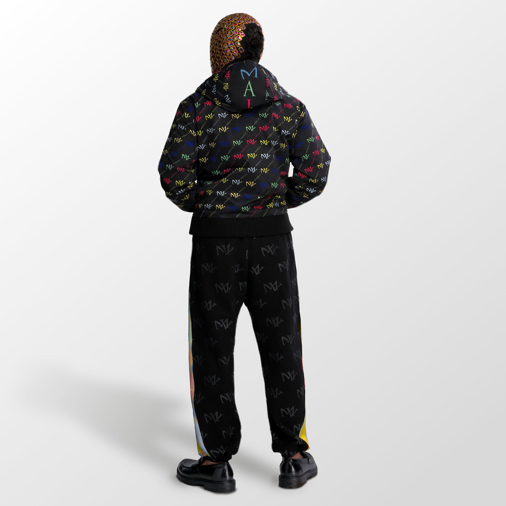 Model wearing the luxury multicolored jacket and joggers with 'MV' branding and geometric shapes from 'MAIVUS' against a white studio backdrop
