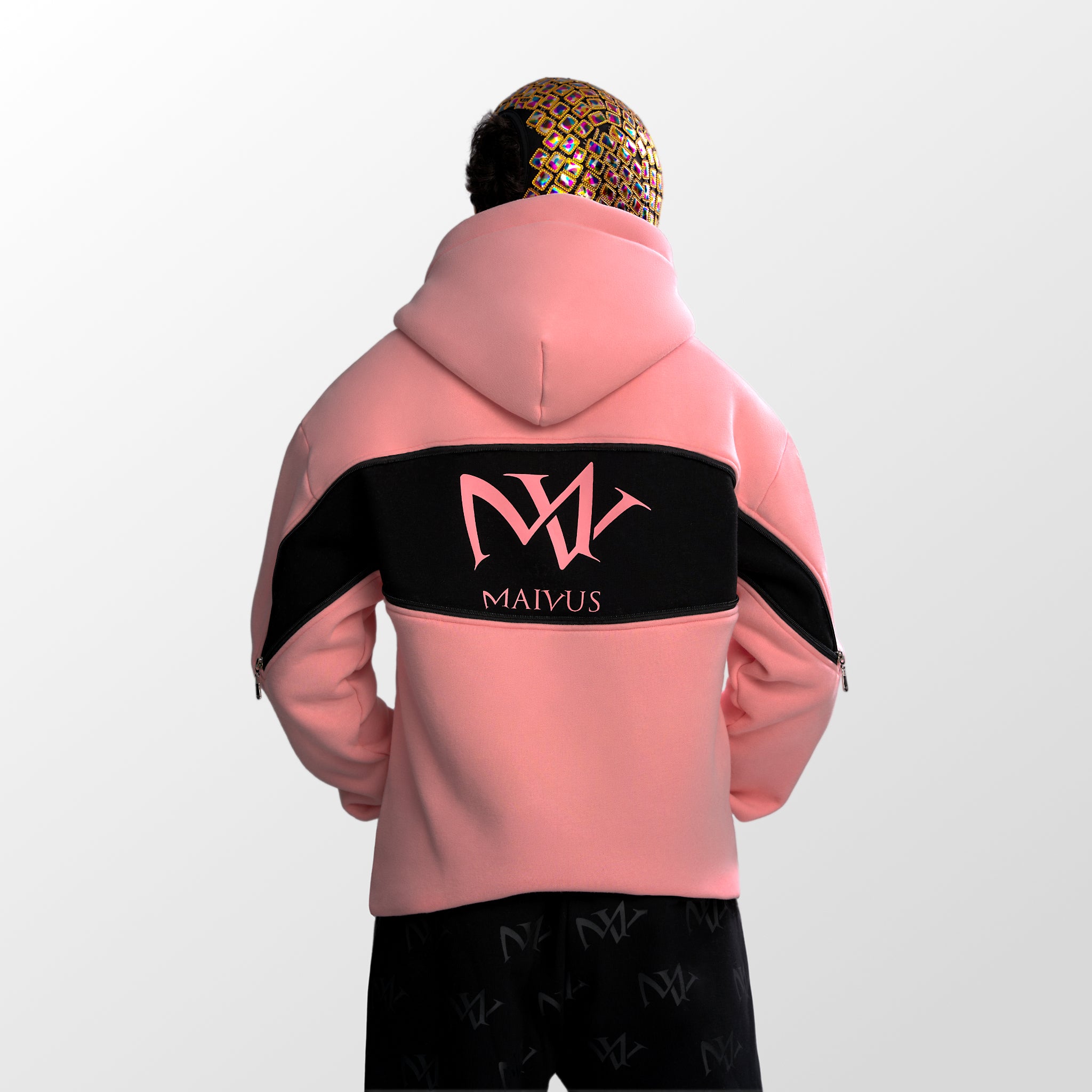 Model wearing a pink and black luxury hoodie. Large 'MV' logo on back of hoodie from 'MAIVUS' against a white studio backdrop