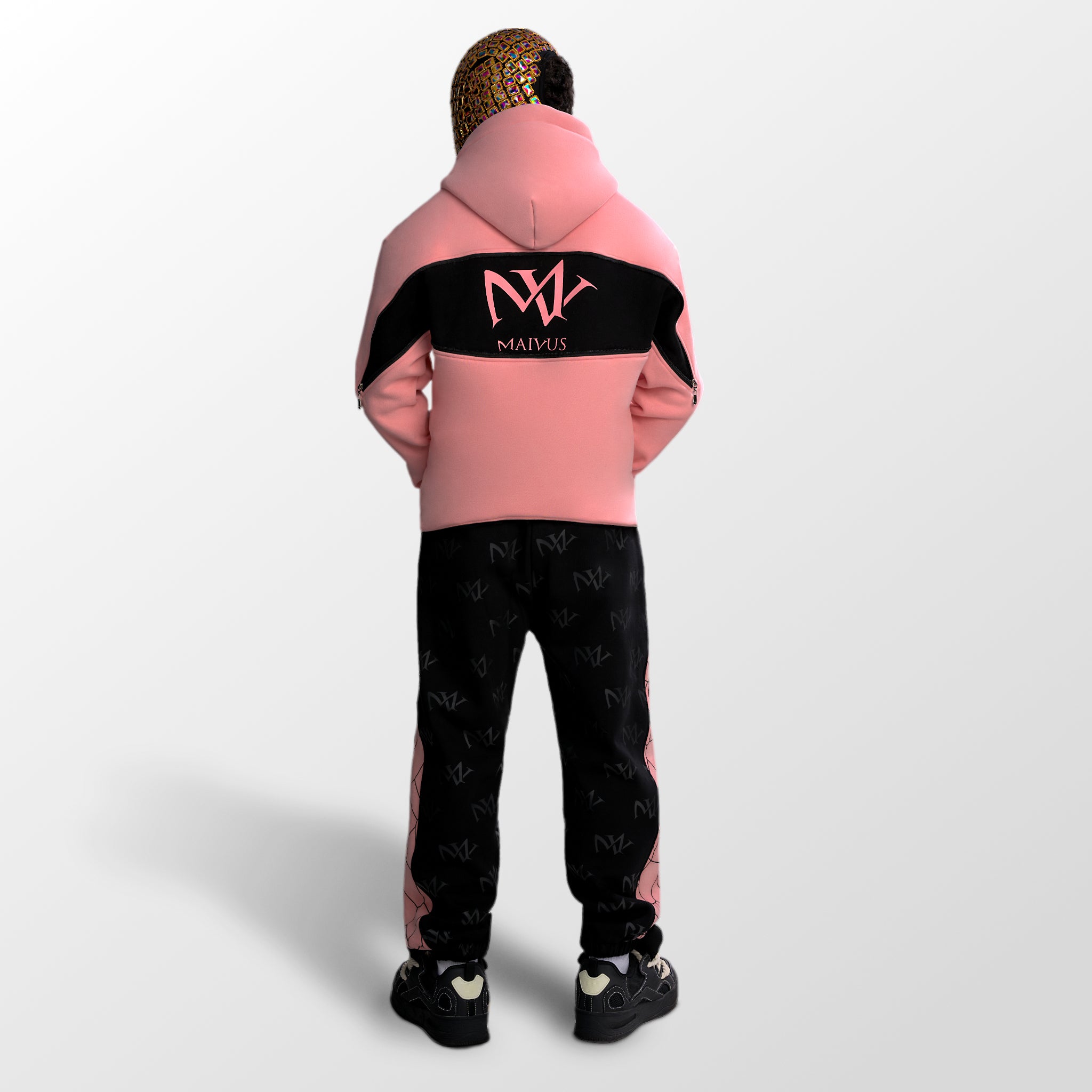 Model wearing a pink and black luxury hoodie and joggers. 'MV' branding all over the joggers and large 'MV' logo on back of hoodie from 'MAIVUS' against a white studio backdrop