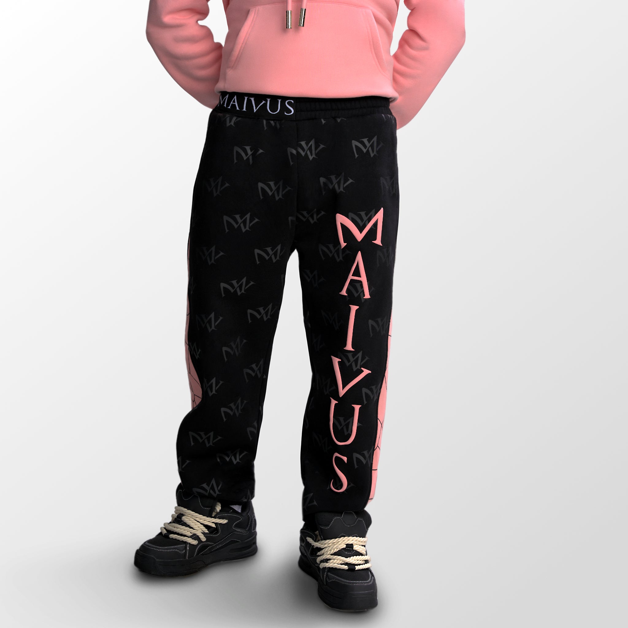 Model wearing the luxury black and pink joggers with 'MV' branding and geometric shapes from 'MAIVUS' against a white studio backdrop
