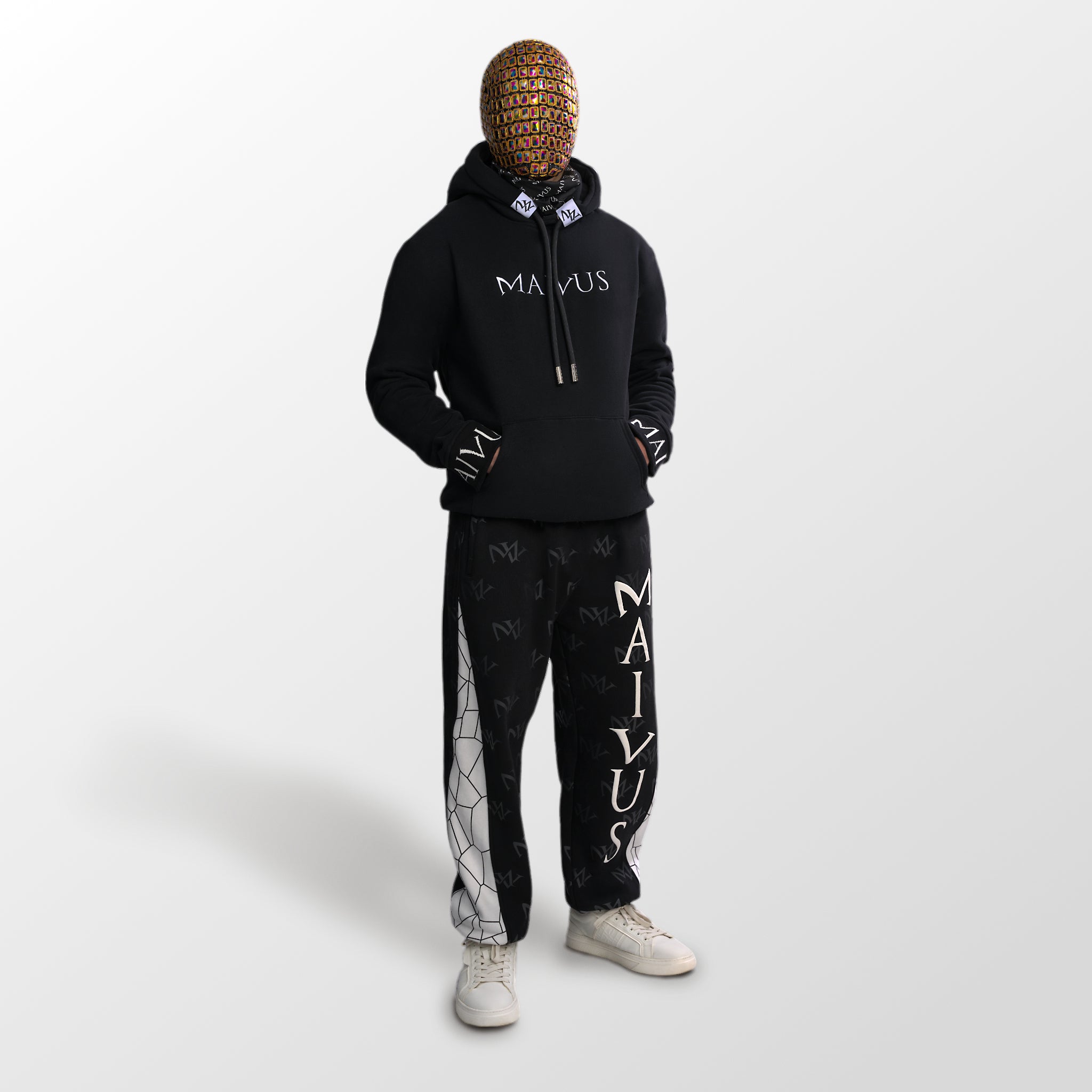 Model wearing a luxury black and white hoodie and joggers. 'MV' branding on joggers with geometric shapes and white embroidery on hoodie from 'MAIVUS' against a white studio 