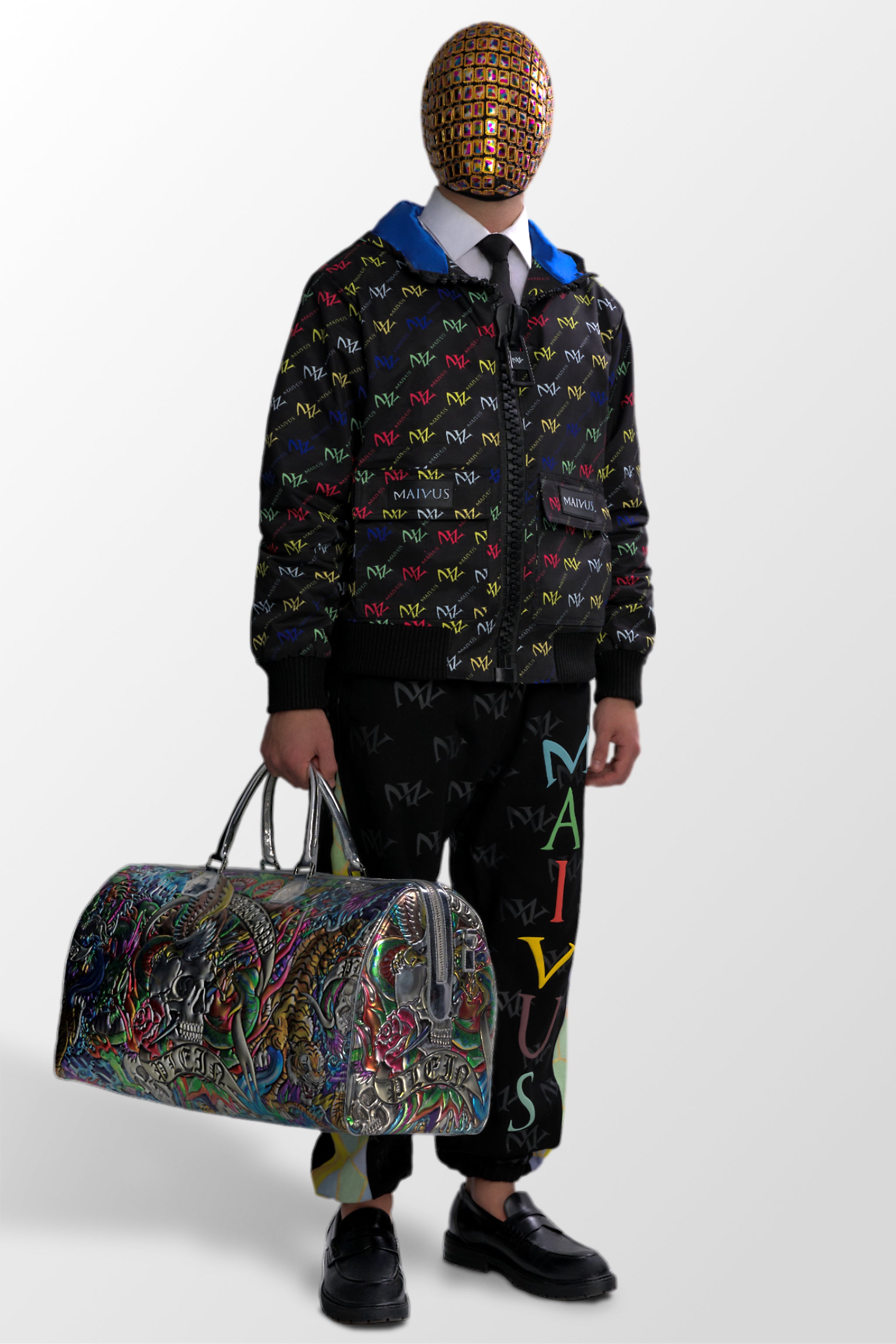 Model wearing the luxury multicolored jacket and joggers with 'MV' branding and geometric shapes from 'MAIVUS' against a white studio backdrop