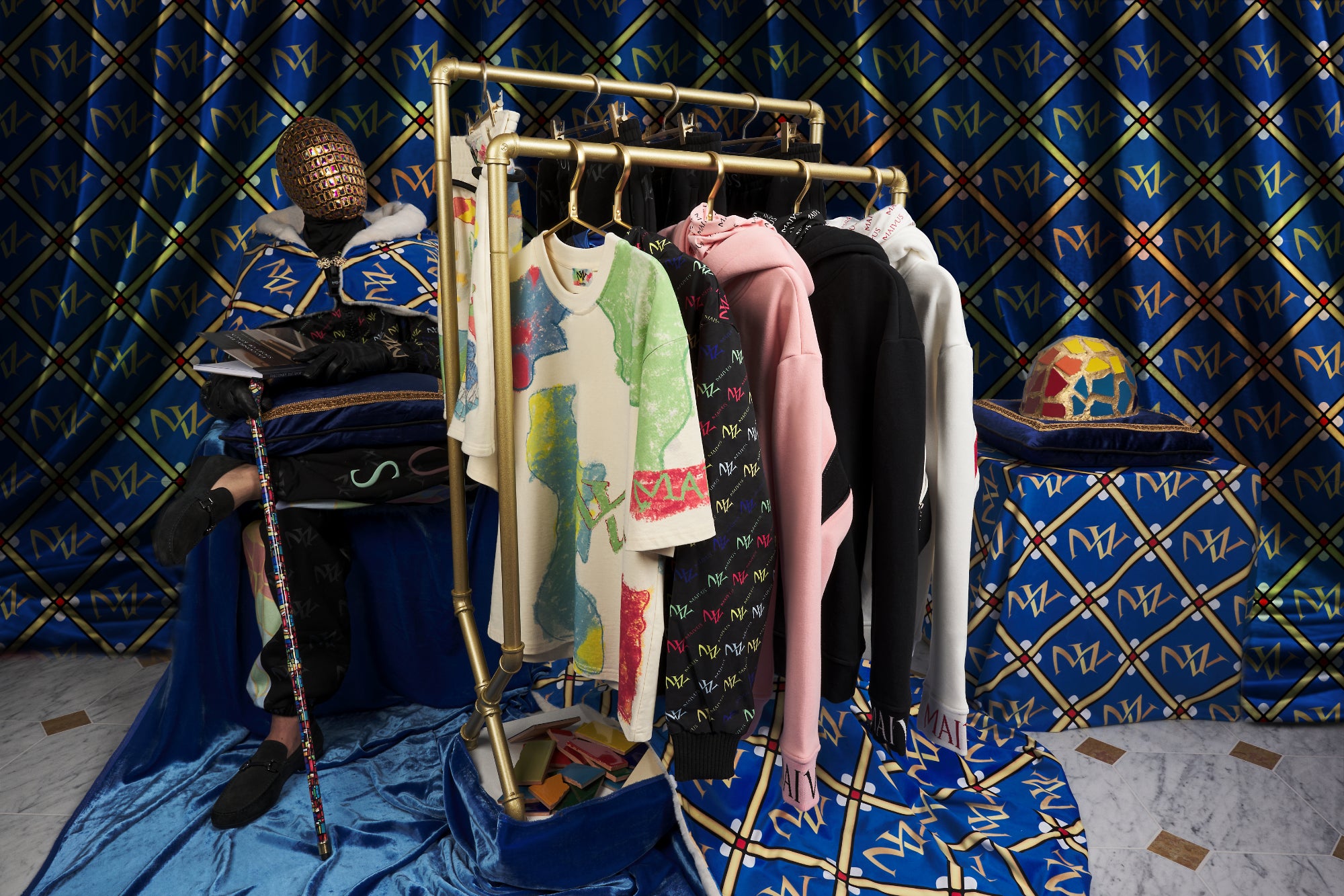 The king of dreams sitting down with 'MAIVUS' branded robe next to a rack of luxury clothing from MAIVUS
